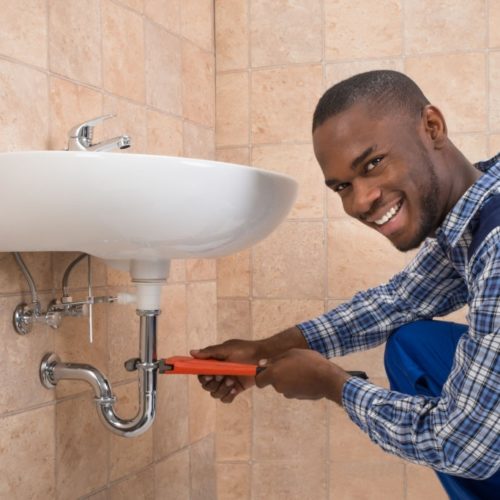 Young African Male Plumber Repairing Sink In Bathroom