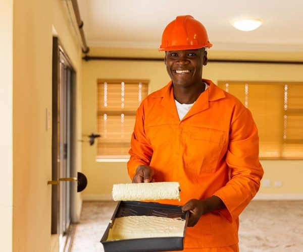 portrait of happy african builder holding paint roller and paint