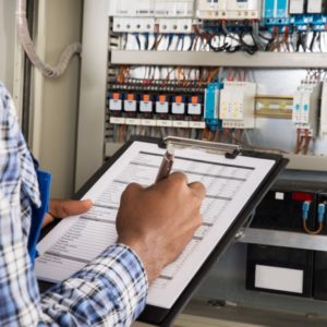 Close-up Of Male Technician Writing On Clipboard In Front Of Fusebox